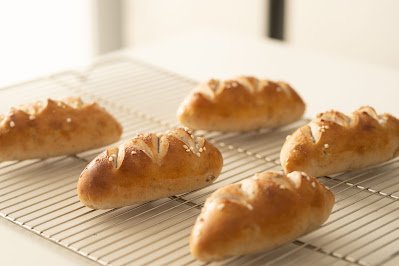 Pãezinhos tipo pretzel artesanais com cortes no topo e sal grosso esfriando sobre grade de metal.