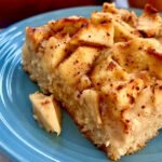 Fatia de bolo de maçã com canela fofinho servida em um prato azul com pedaços da fruta por cima.