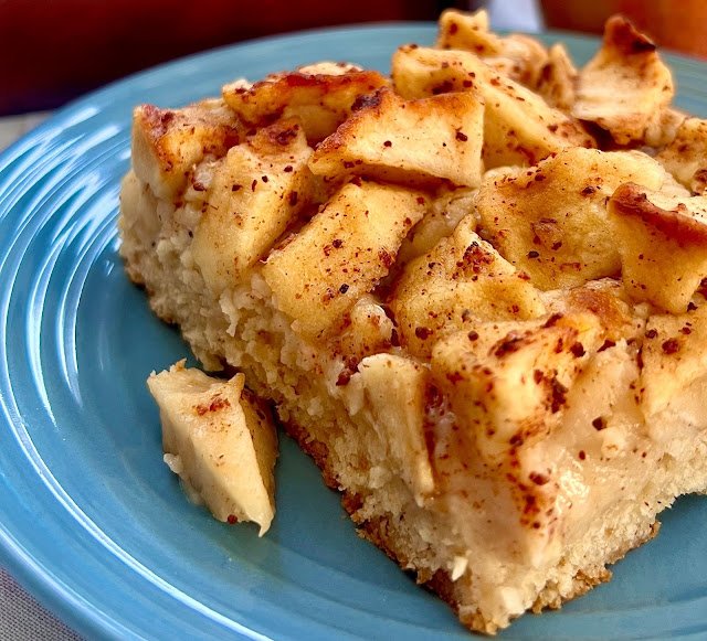 Fatia de bolo de maçã com canela fofinho servida em um prato azul com pedaços da fruta por cima.