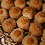 Vários brigadeiros de churros gourmet dispostos em uma bandeja dourada, salpicados com açúcar e canela, e finalizados com uma pitanga de doce de leite.