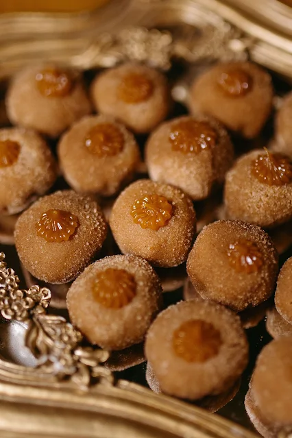 Vários brigadeiros de churros gourmet dispostos em uma bandeja dourada, salpicados com açúcar e canela, e finalizados com uma pitanga de doce de leite.