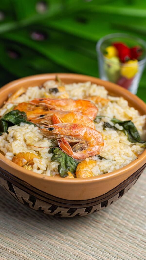 Tigela rústica de barro cheia de arroz paraense cremoso com tucupi, folhas verdes de jambu e camarões grelhados inteiros no topo.