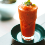 Copo de suco de acerola cremoso, vermelho e servido gelado.
