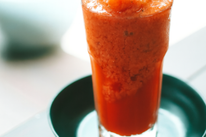 Copo de suco de acerola cremoso, vermelho e servido gelado.