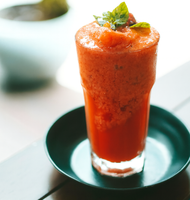 Copo de suco de acerola cremoso, vermelho e servido gelado.