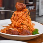 Macarrão espaguete com almôndegas de carne ao molho de tomate com cogumelos e queijo ralado.
