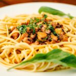 Prato de macarrão ao alho com frango em cubos dourados e folhas frescas de espinafre.