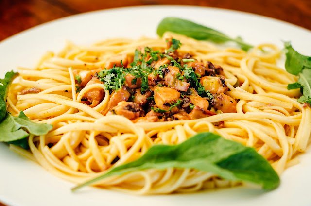 Prato de macarrão ao alho com frango em cubos dourados e folhas frescas de espinafre.