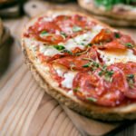Mini pizzas feitas com pão francês, cobertas com molho de tomate, queijo derretido e ingredientes variados.