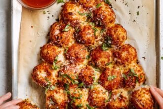 Pão de alho puxa-puxa em formato de árvore de Natal, com bolinhas douradas, queijo parmesão, ervas e molho para acompanhar.
