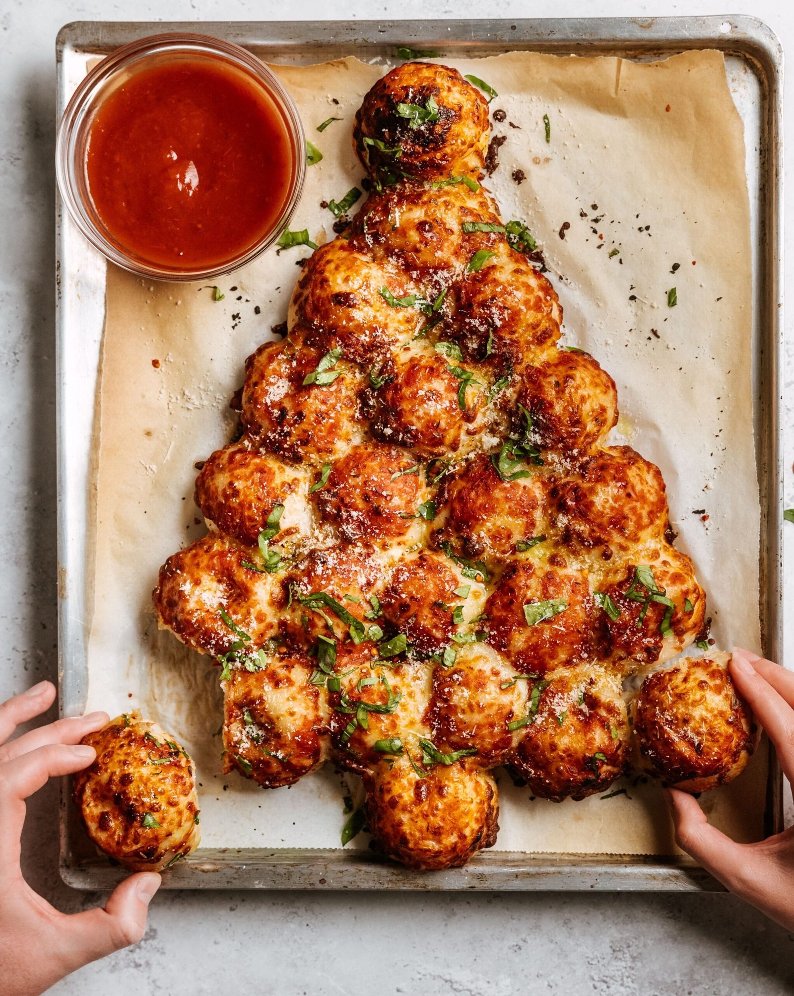 Pão de alho puxa-puxa em formato de árvore de Natal, com bolinhas douradas, queijo parmesão, ervas e molho para acompanhar.