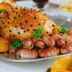 Mesa de ceia de Natal simples com pratos caseiros, acompanhamentos, bolo e bebida festiva.